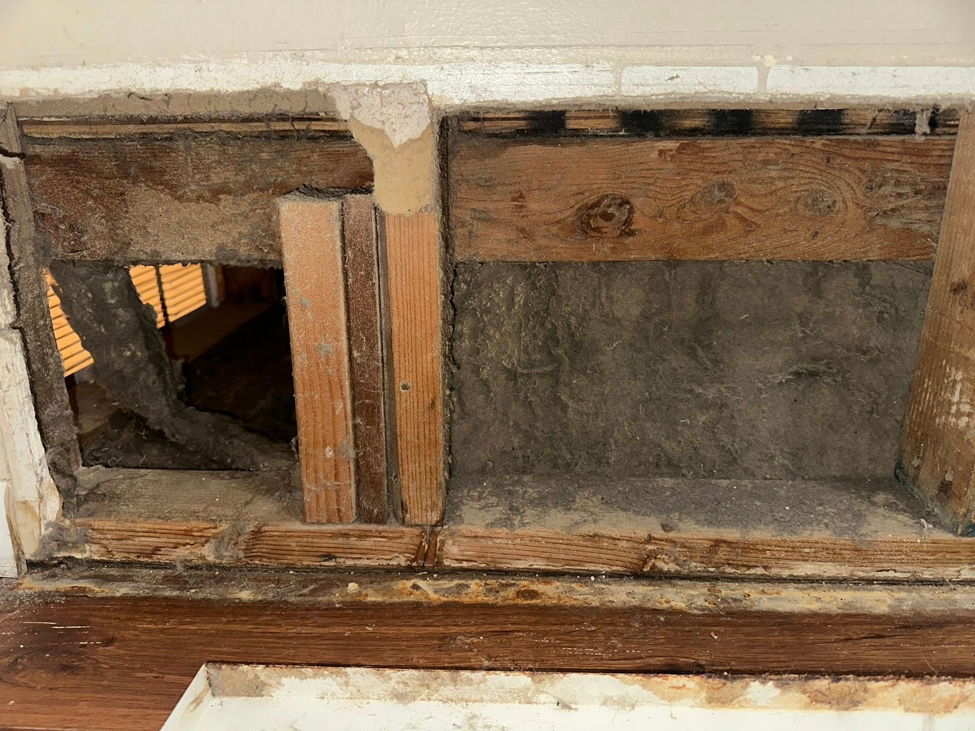 Wooden air vent in wall, damaged with exposed inner structure and dark gray cement.
