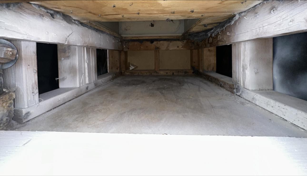 Interior view of a rectangular, light-colored concrete structure with wooden beams and dark openings.