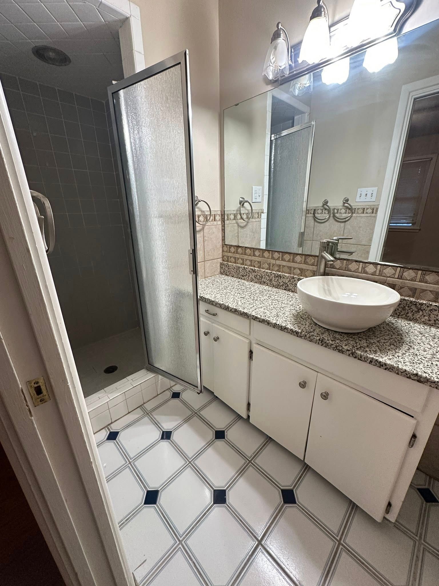 Bathroom with white cabinets, stone countertop, bowl sink, and patterned floor.