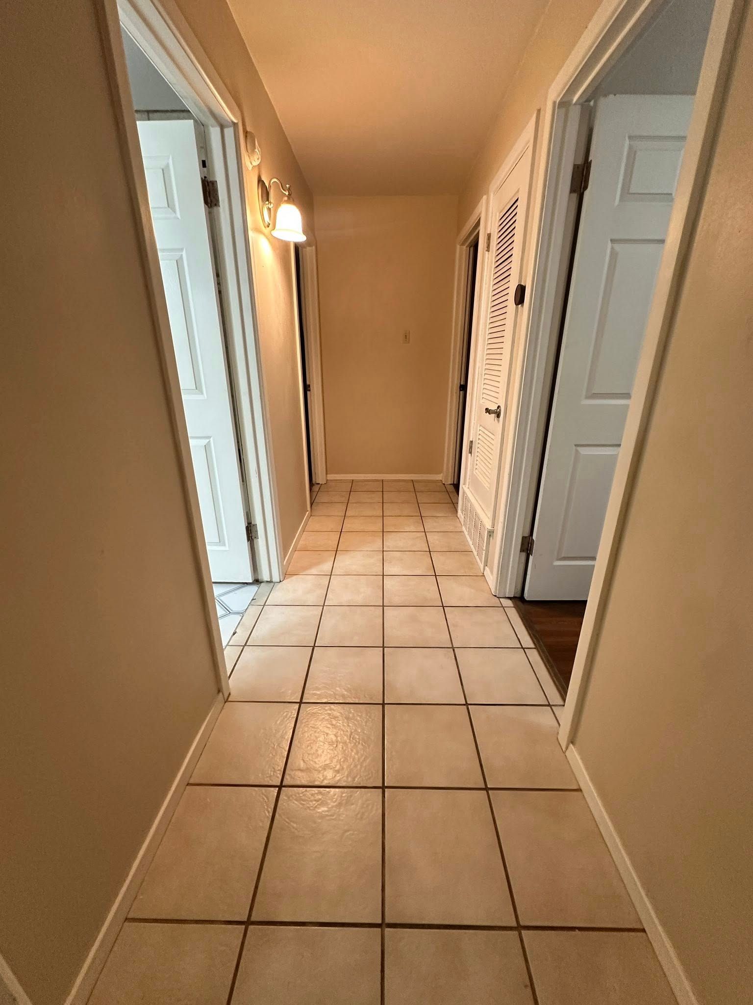 Narrow hallway with tiled floor, doors on both sides, and a light fixture.
