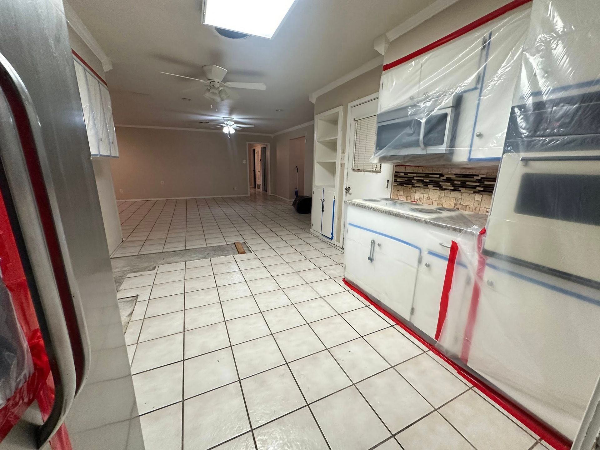 Kitchen with white cabinets covered in plastic for renovation; tiled floor, open to living space.