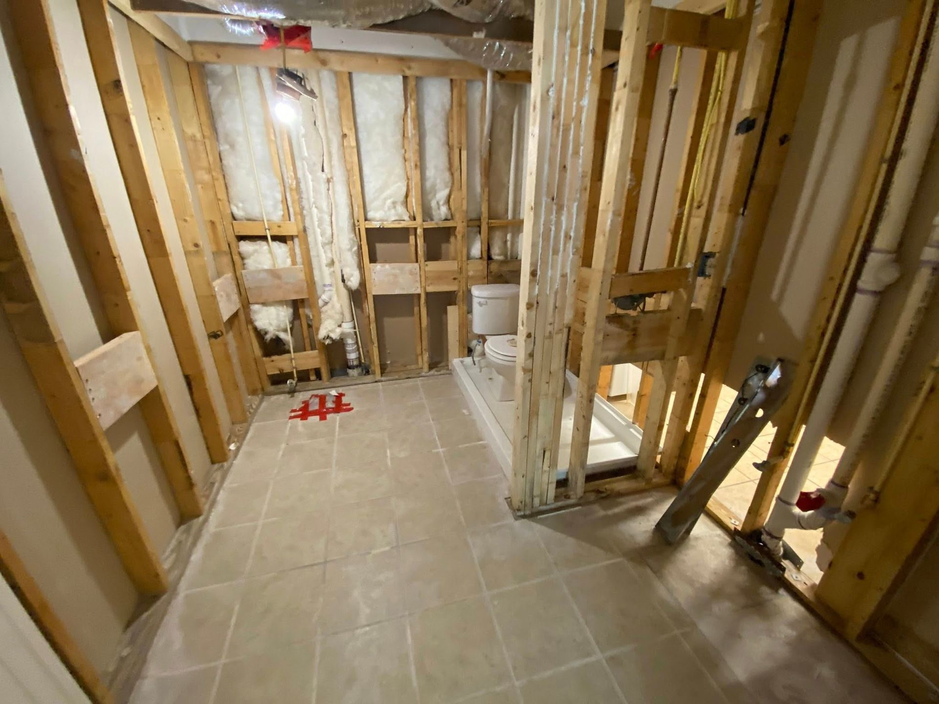 Bathroom under construction: wood framing, insulation, tiled floor. Plumbing visible.