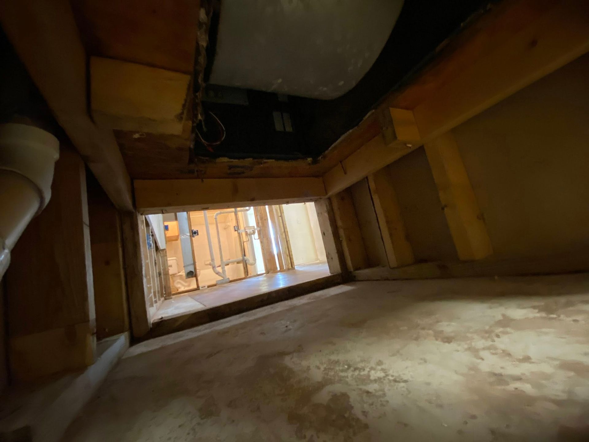 View from inside a crawl space, showing wooden framing, ductwork, and partially exposed wall.