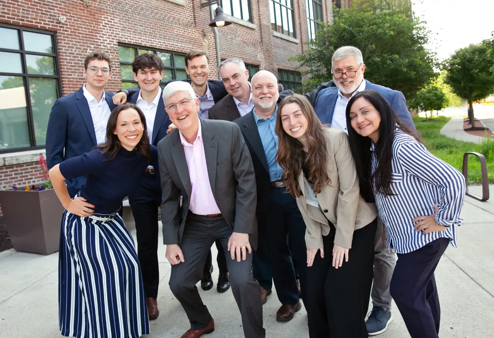 Group of people smiling, posing outdoors near a brick building.