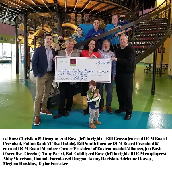 Group of people holding a large check at an indoor playground.