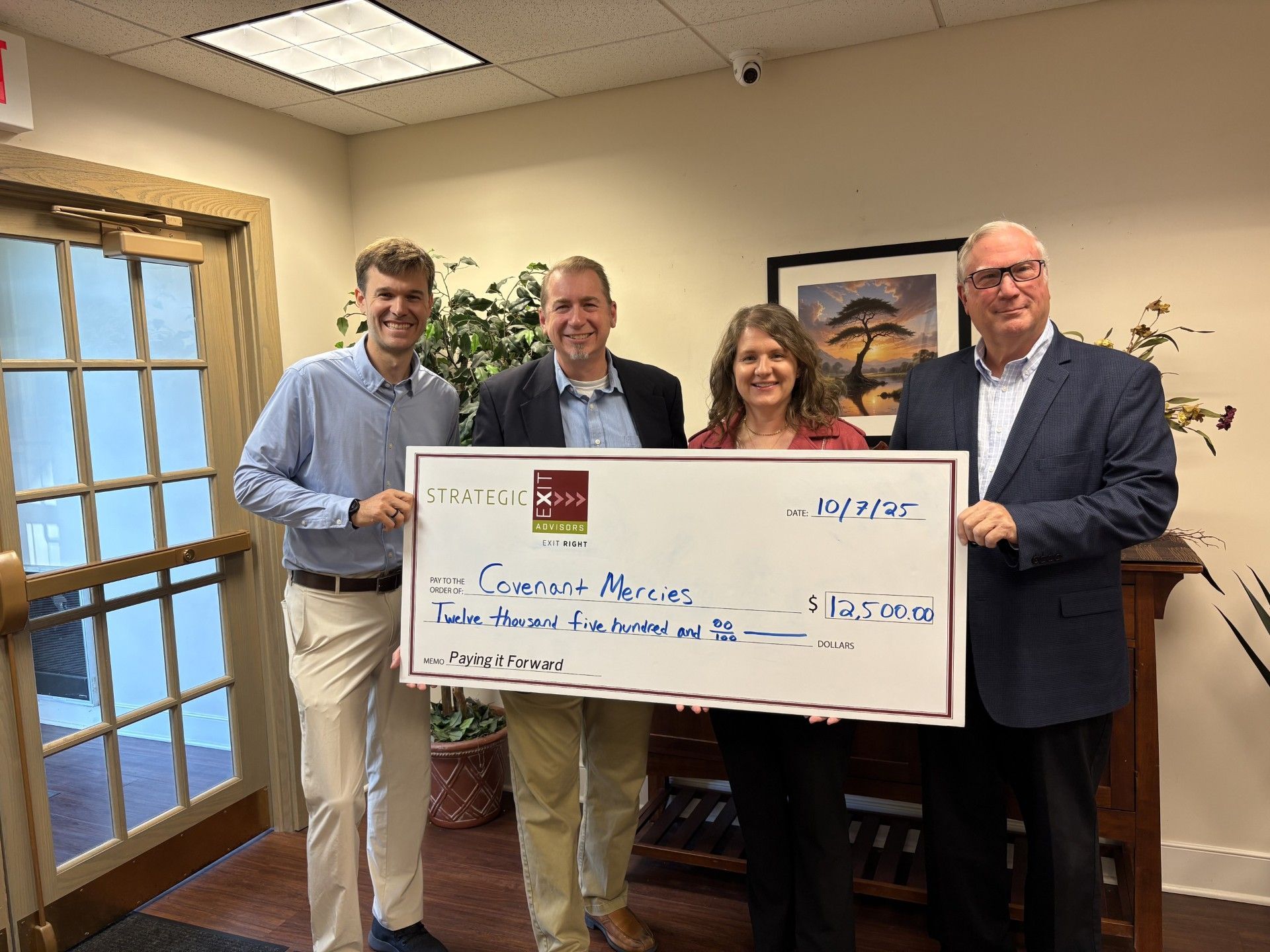 Four people holding a large check in an office setting.