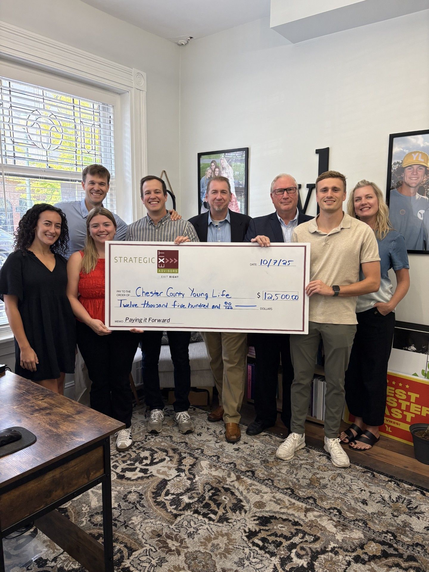 Group of people holding a large check in an office, smiling.