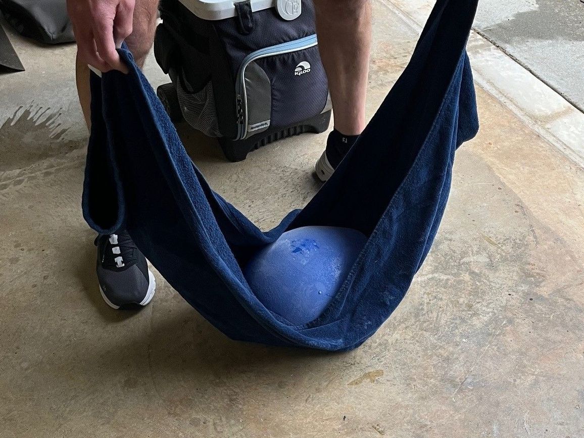 Person holding a blue towel with a large, blue ball inside. The setting is outdoors.