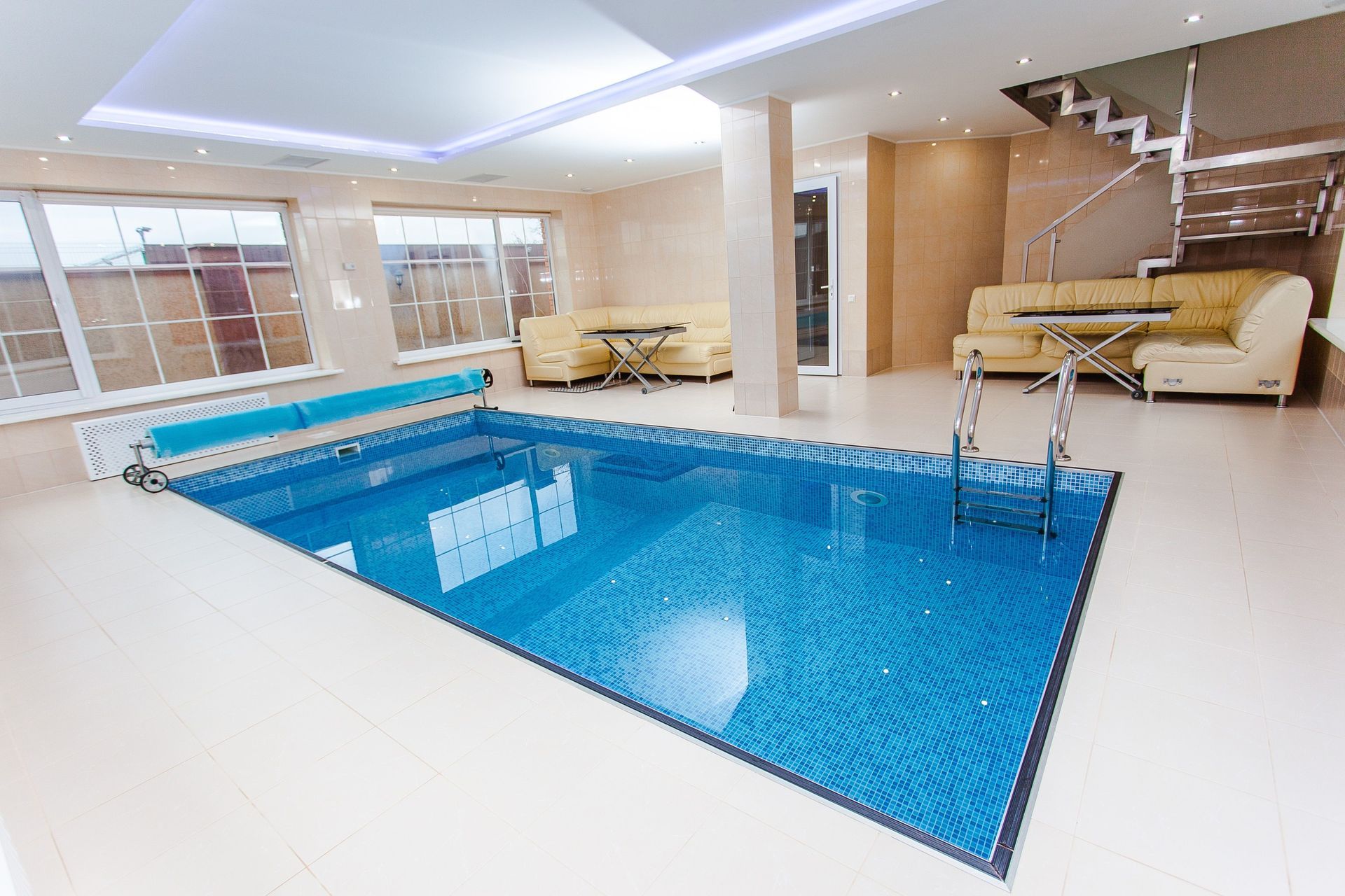 Indoor luxury pool with blue water, white tile, and a lounge area beside stairs