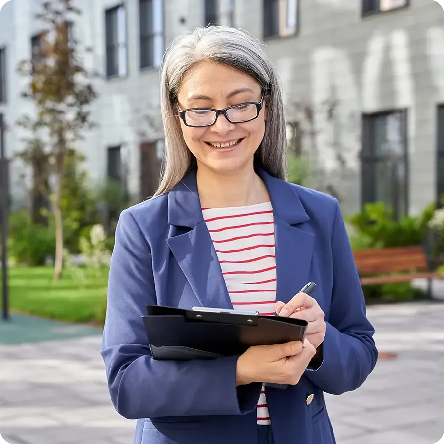 Attentive businesswoman smiling while looking at clipboard in her hands while standing outside in the street