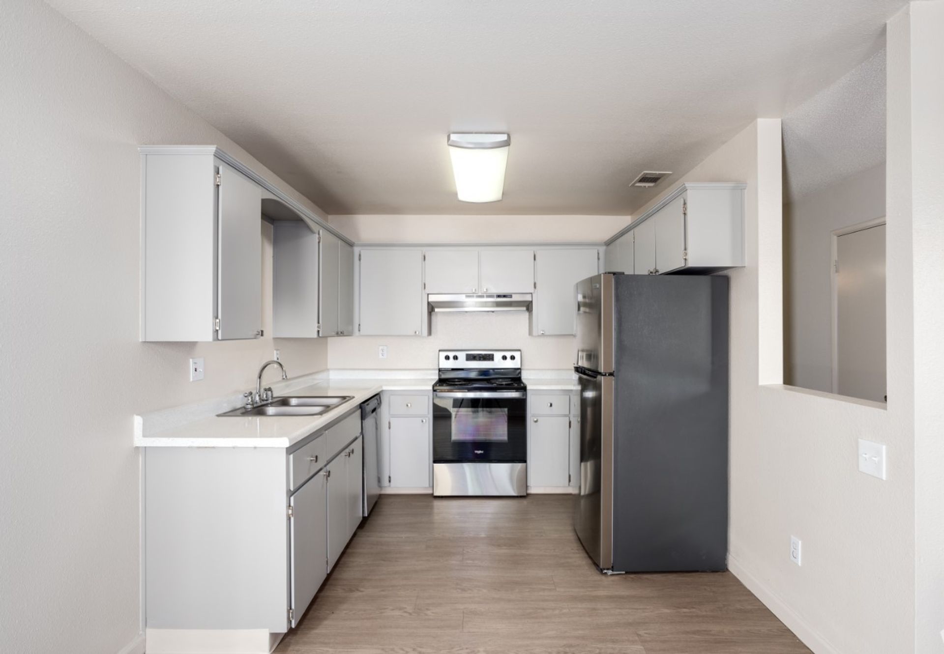 Bright white galley kitchen with gray cabinets, stainless stove, and dark refrigerator.
