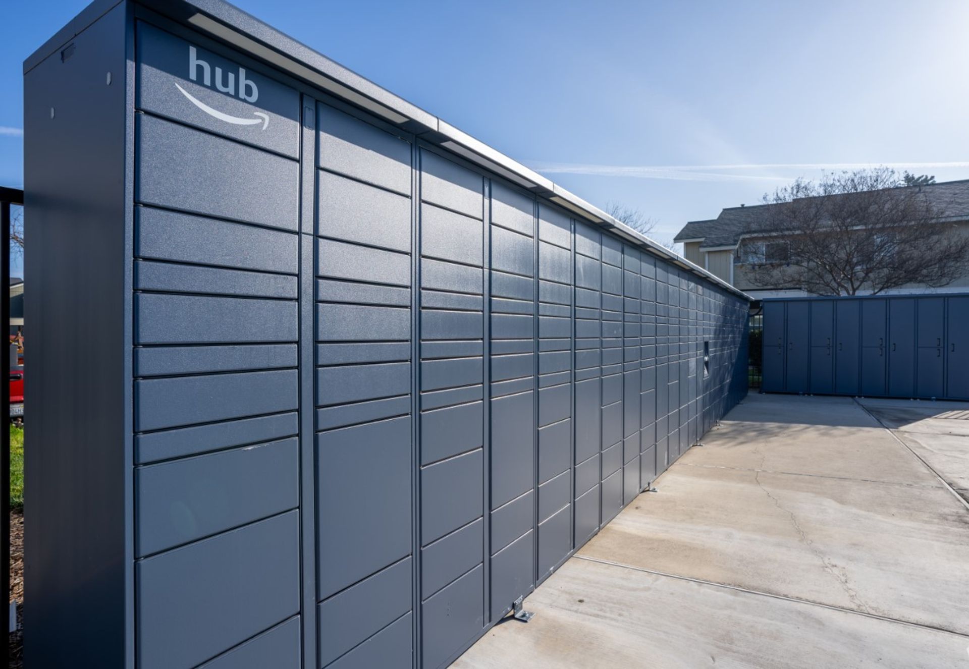 Row of gray outdoor storage lockers along a concrete walkway on a sunny day