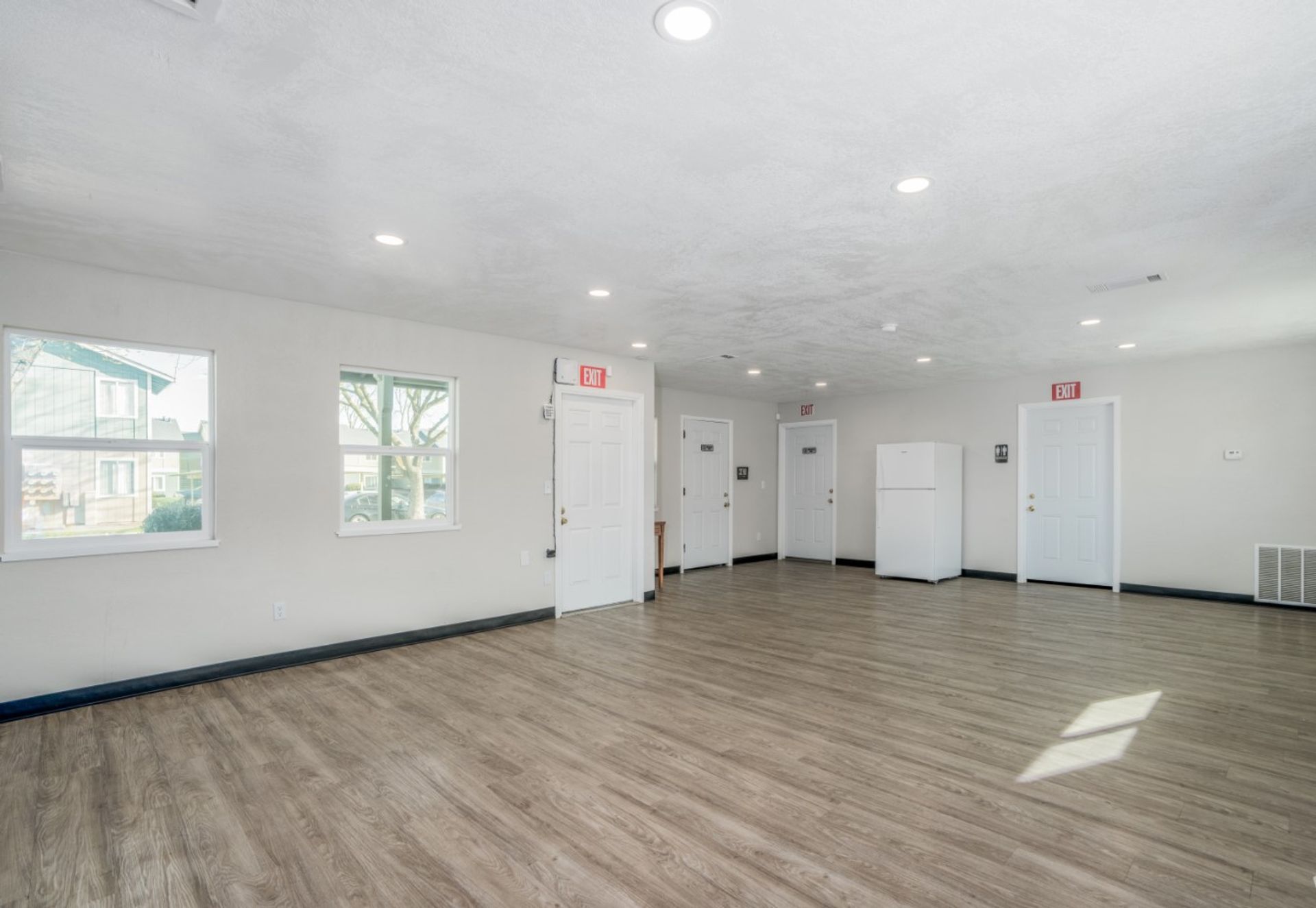 Empty white room with wood-look floors, windows, and recessed ceiling lights