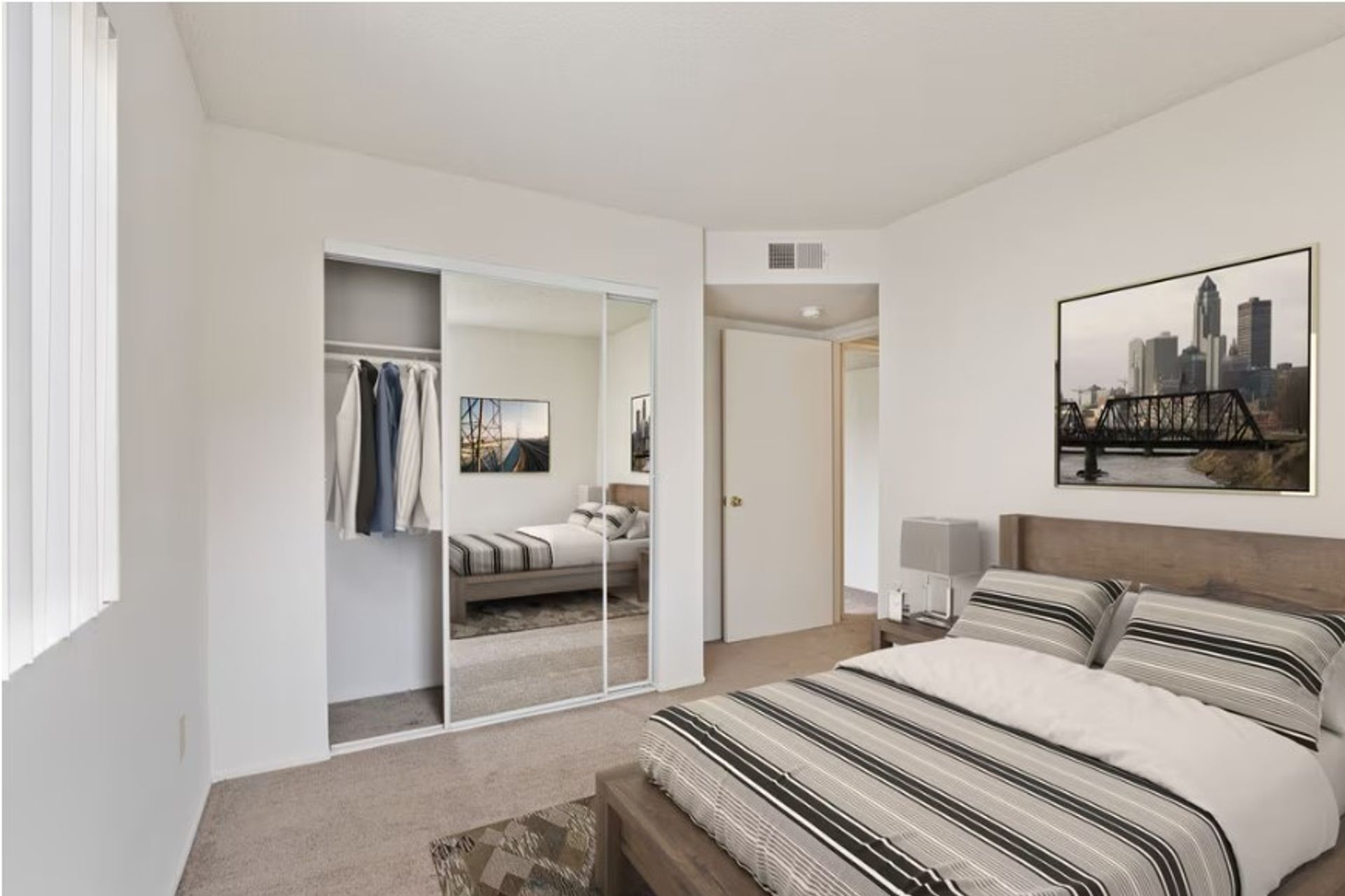 Bright modern bedroom with a striped bedspread, mirrored closet, and cityscape wall art