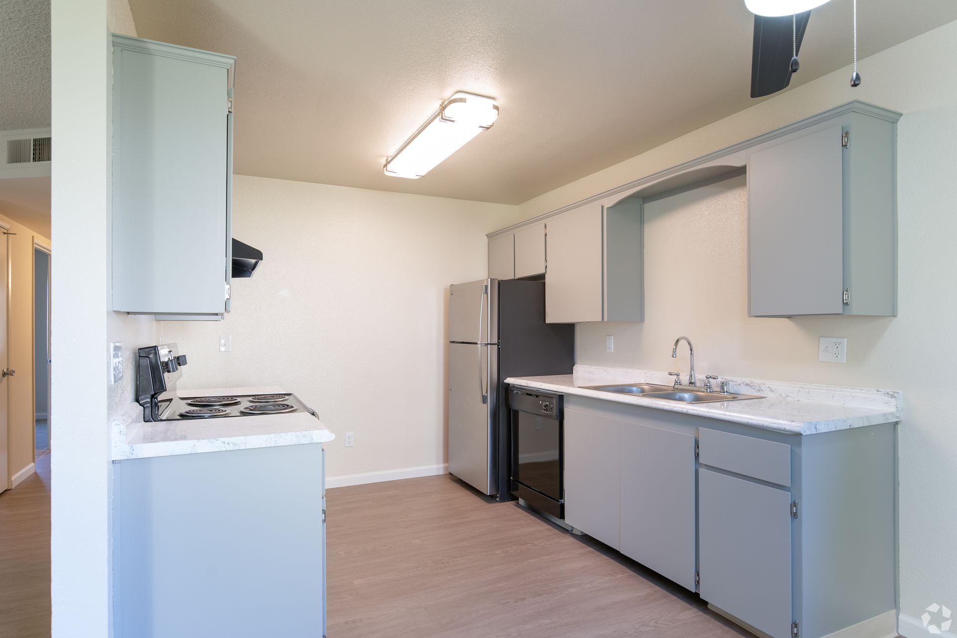 Empty modern kitchen with light gray cabinets, white countertops, and a stainless-steel refrigerator.