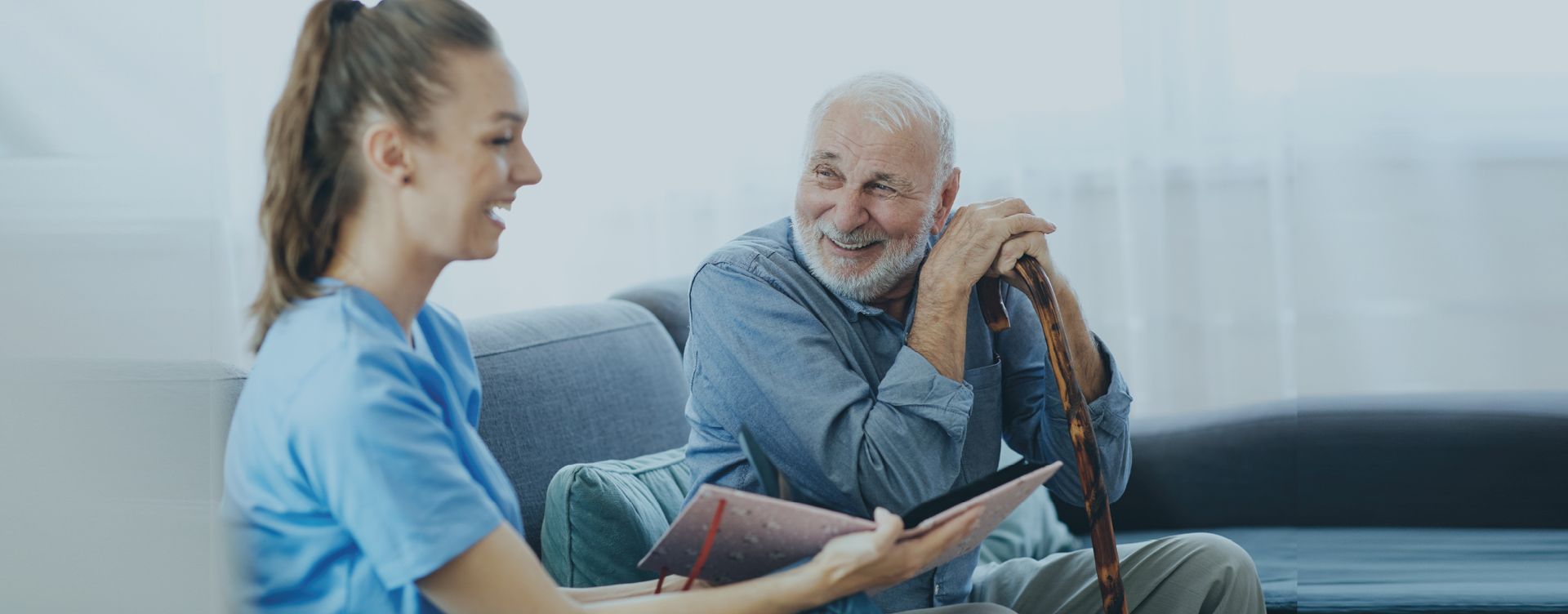 A nurse is talking to an elderly man sitting on a couch.