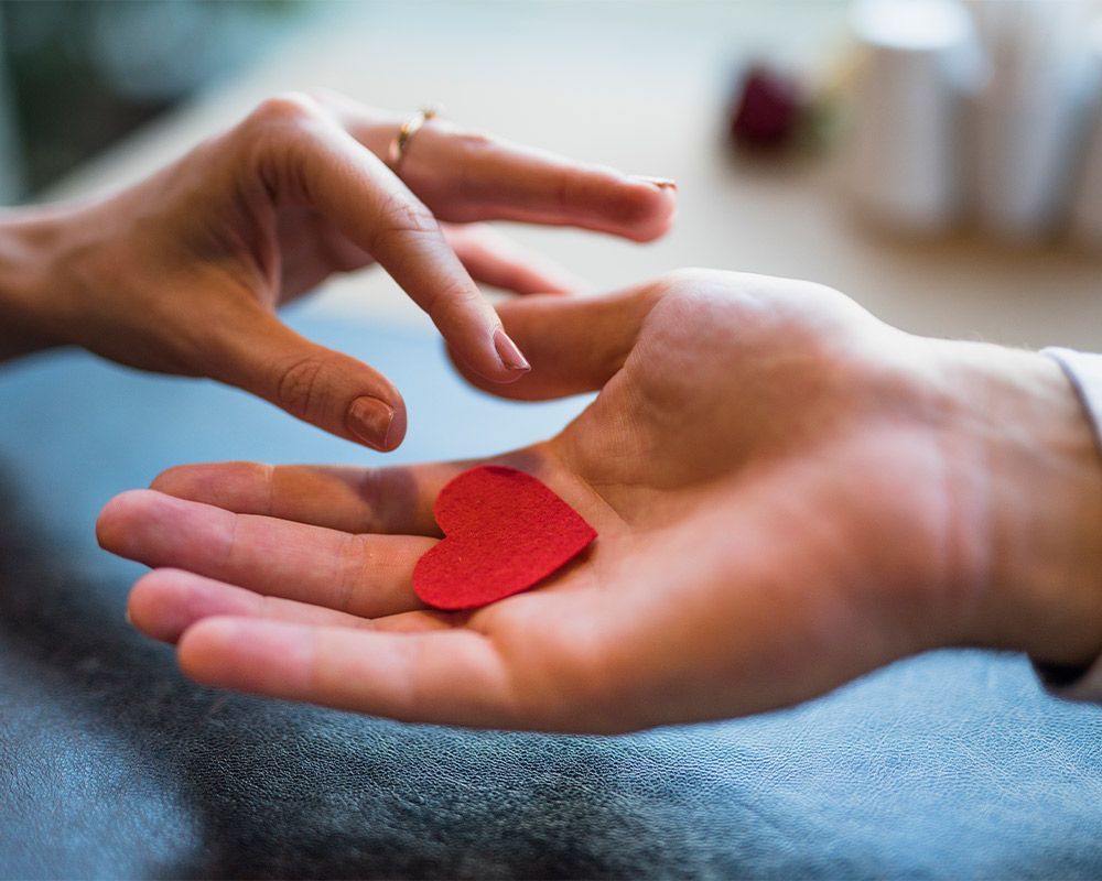 A person is holding a red heart in their hand.