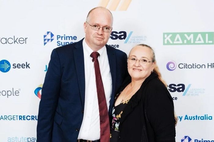 A man and a woman are posing for a picture in front of a wall with logos for companies like seek and kamal