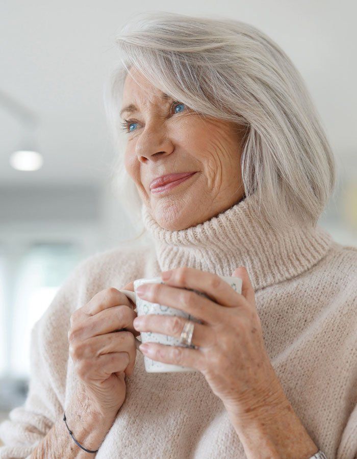 Elderly woman with blue eyes holding coffee cup and smiling while looking to the side