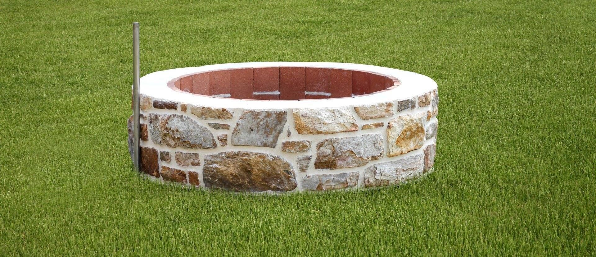 A stone fire pit is sitting in the middle of a lush green field.