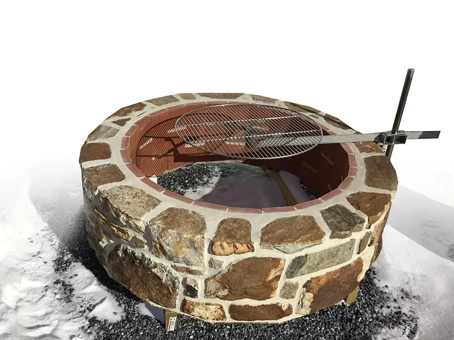 A stone fire pit with a grill inside of it in the snow.