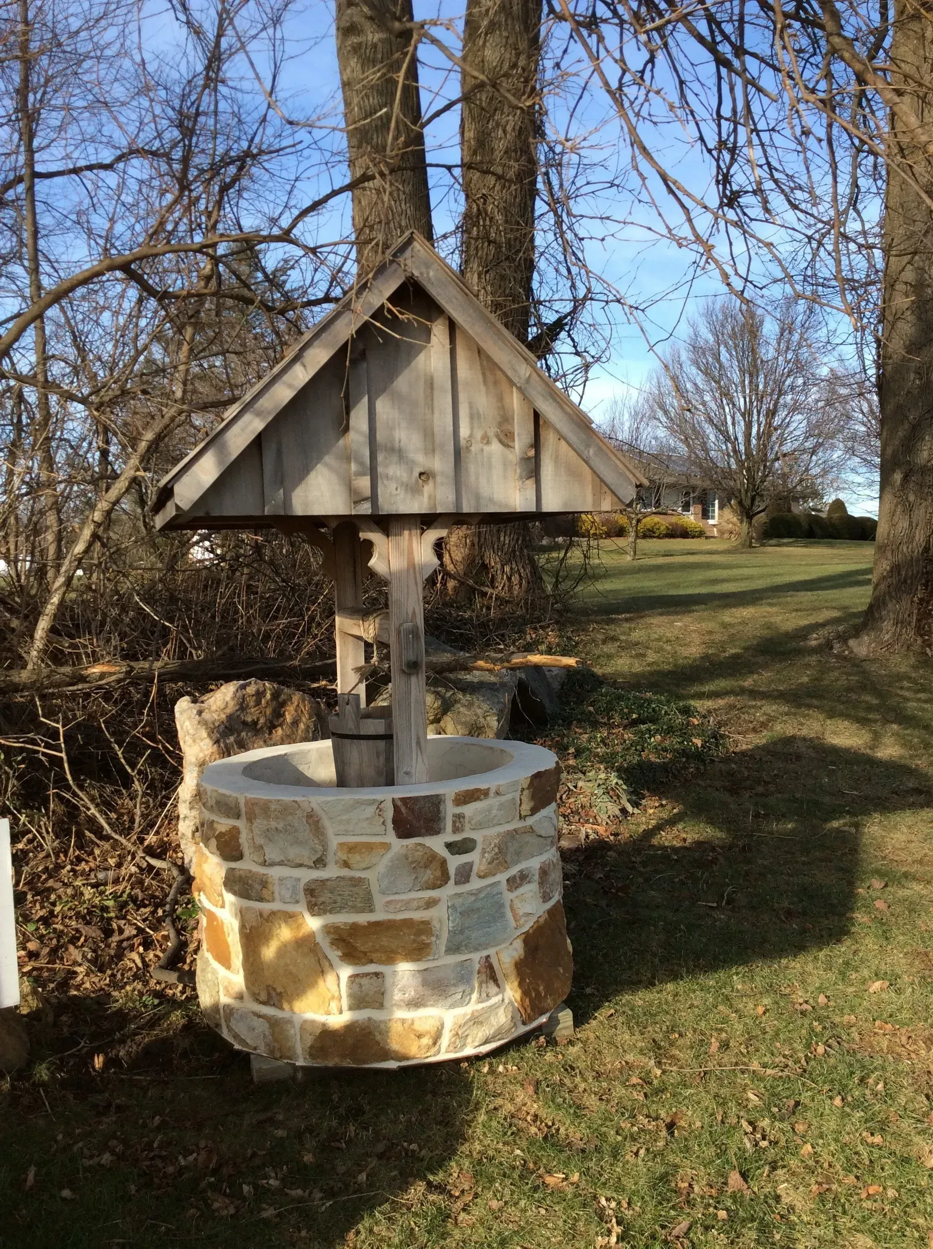 A stone well with a wooden roof is in the middle of a grassy field.