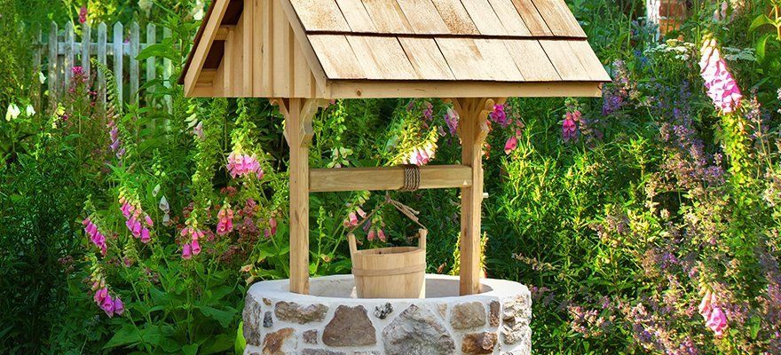 A well with a wooden roof and a wooden bucket in a garden.