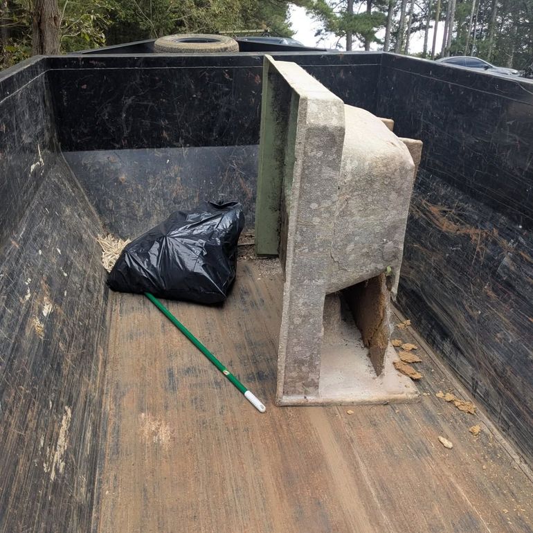 Inside of a black dump truck, a concrete structure, black trash bag, and green pole.
