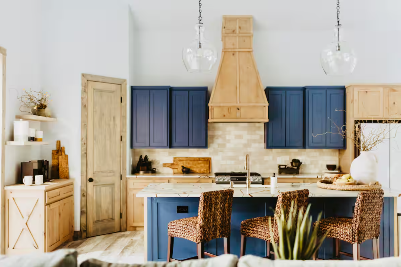 Kitchen with blue and wood cabinets, island, woven chairs, and wooden range hood.