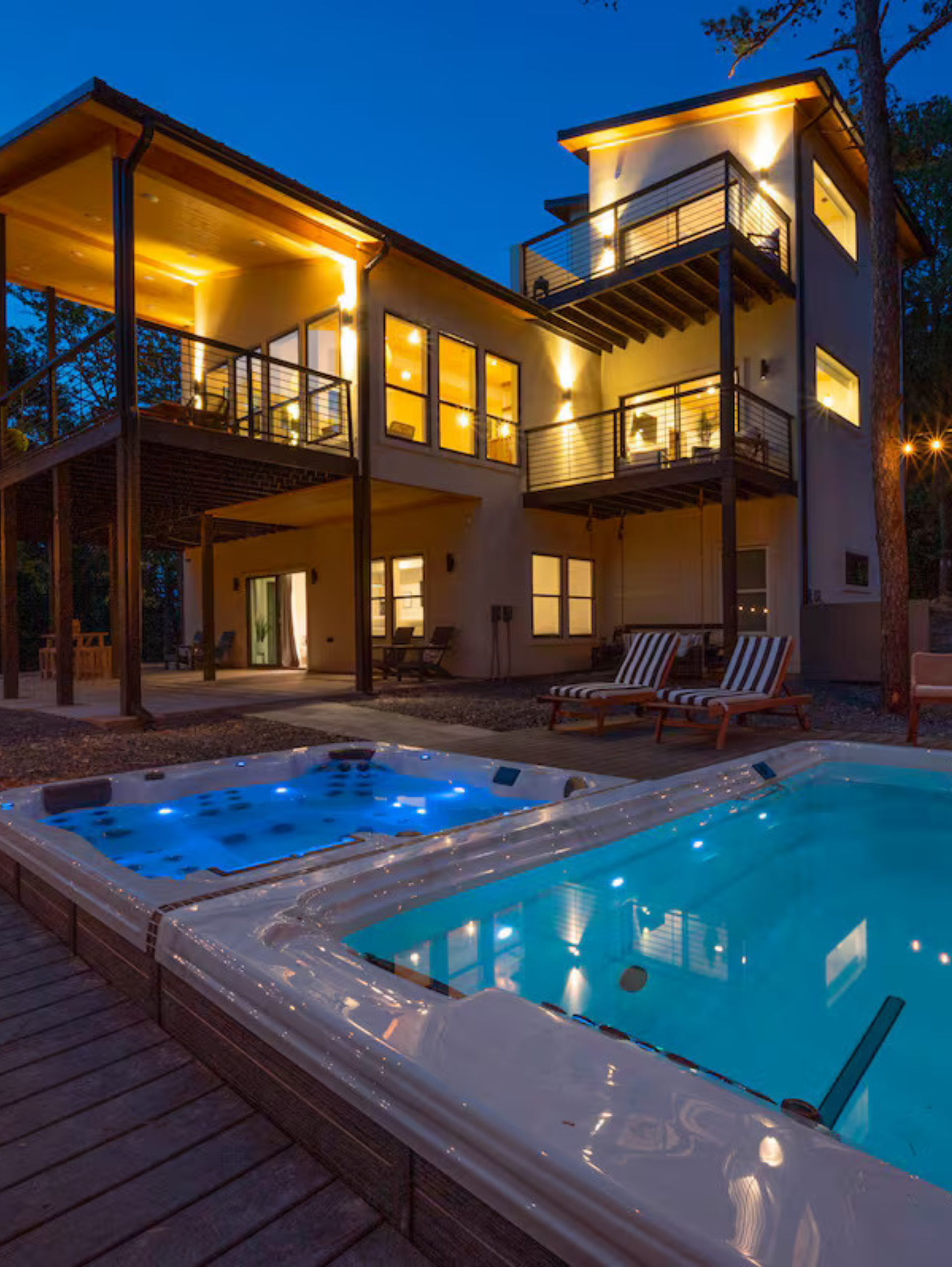Luxury home with illuminated pool and hot tub, multiple balconies, and a night sky backdrop.