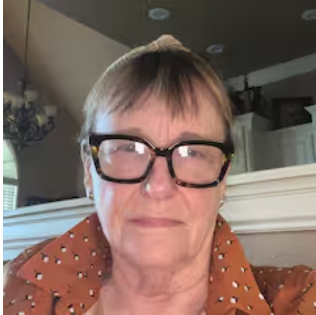 Woman with glasses and short hair, wearing a brown patterned shirt, indoors.