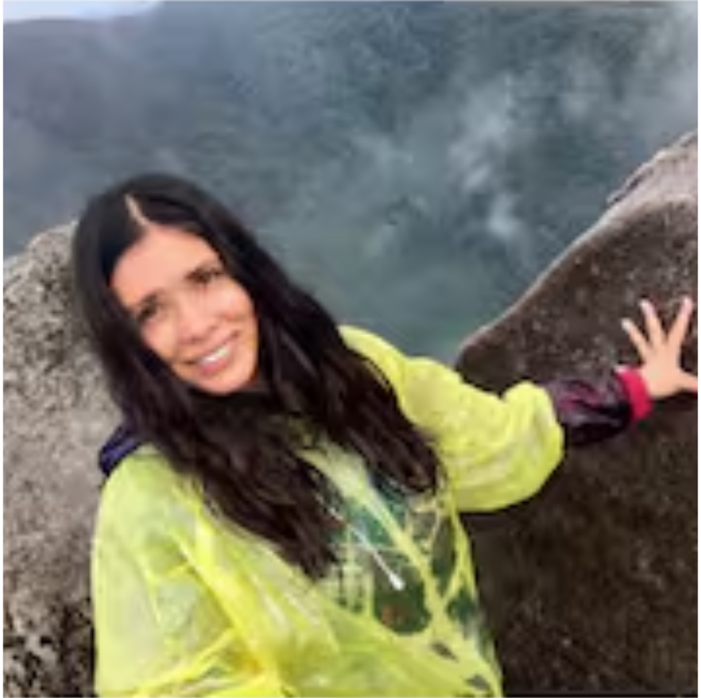 Woman in a yellow raincoat smiles next to a rocky outcropping, hazy background.