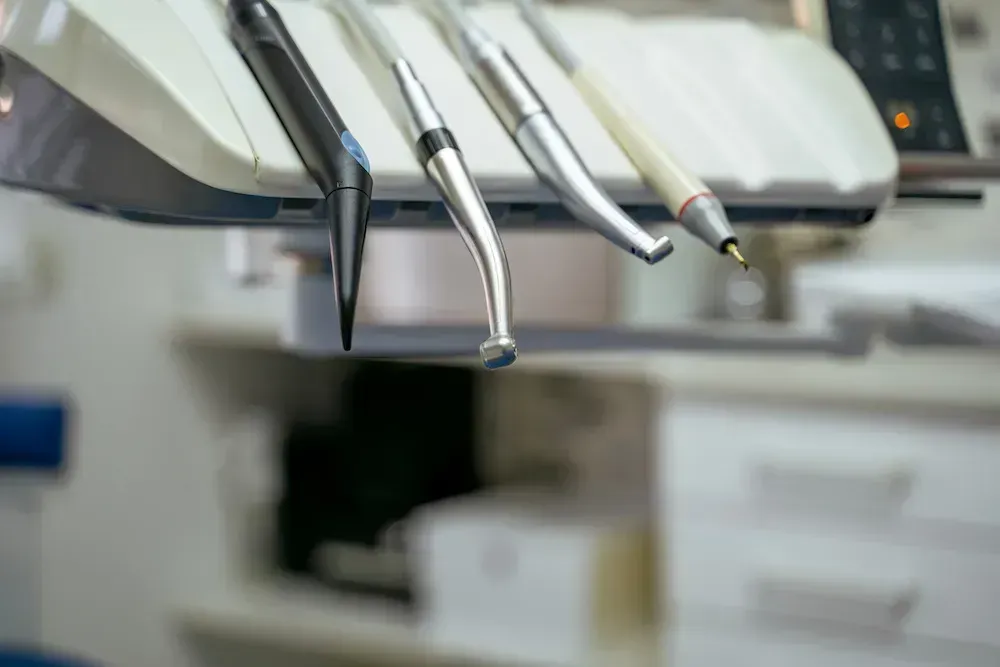 A close up of a dental chair with dental instruments hanging from it.