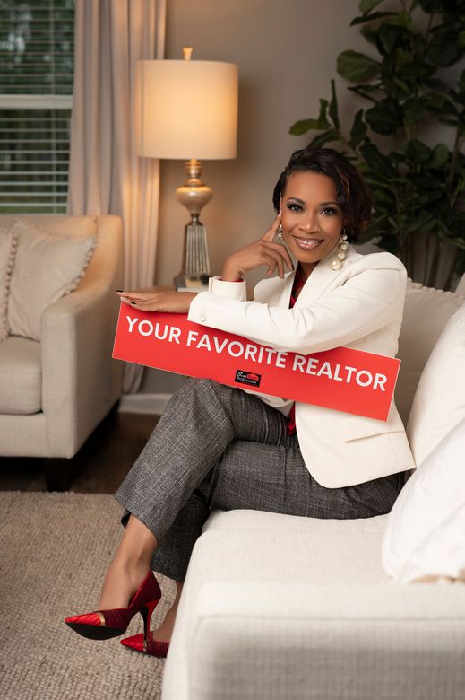 A woman is sitting on a couch holding a sign that says `` your favorite realtor ''.