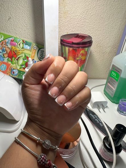 Hand with French tip manicure; various nail supplies and accessories in the background.