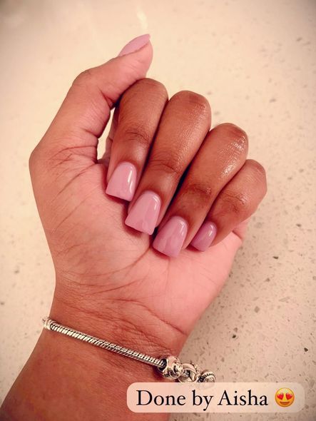 A hand with square, pink gel nails rests on a surface; a silver bracelet is visible.