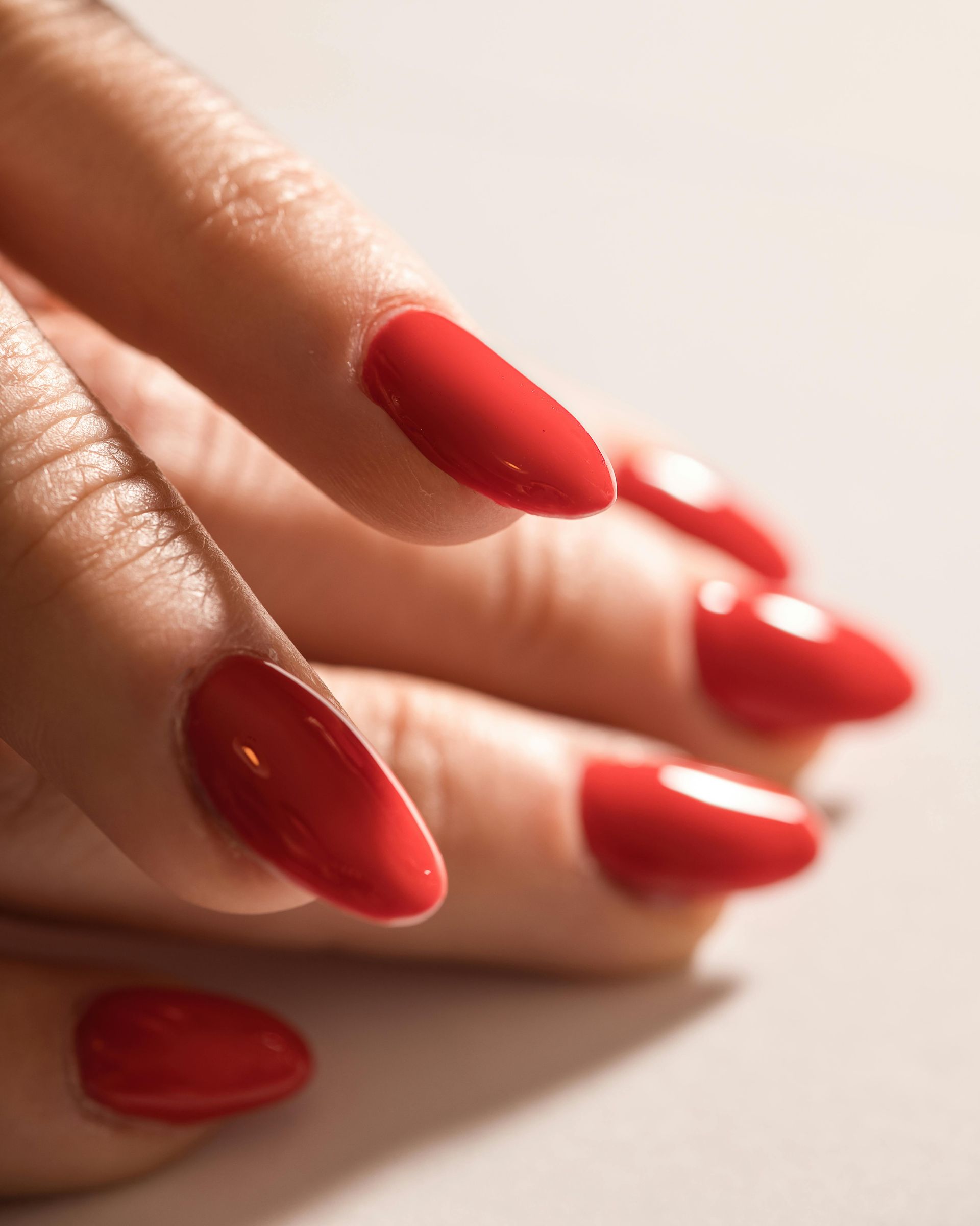 Hand with red, glossy, almond-shaped nails on a light background.