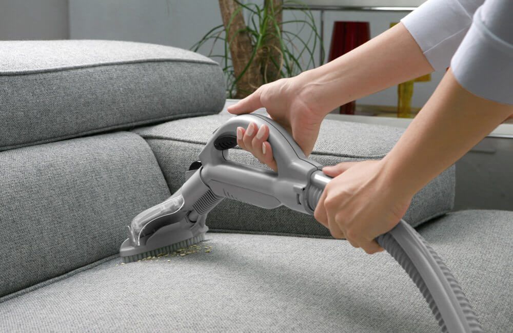 A person is cleaning a couch with a vacuum cleaner