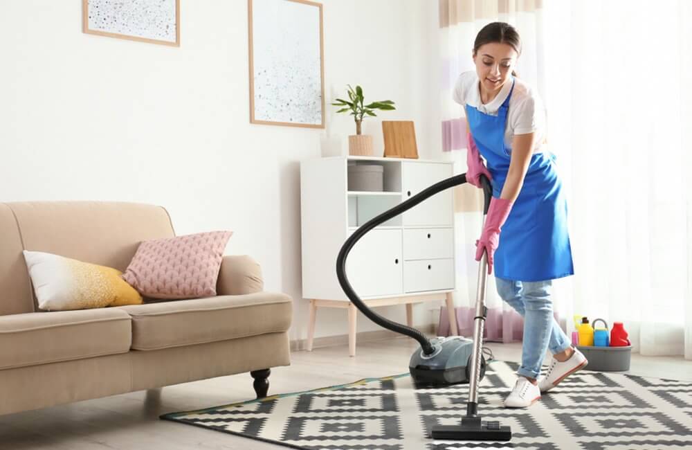 A woman is cleaning the floor with a vacuum cleaner in a living room.