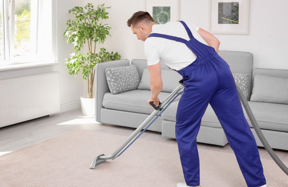A man is using a vacuum cleaner to clean a carpet in a living room.