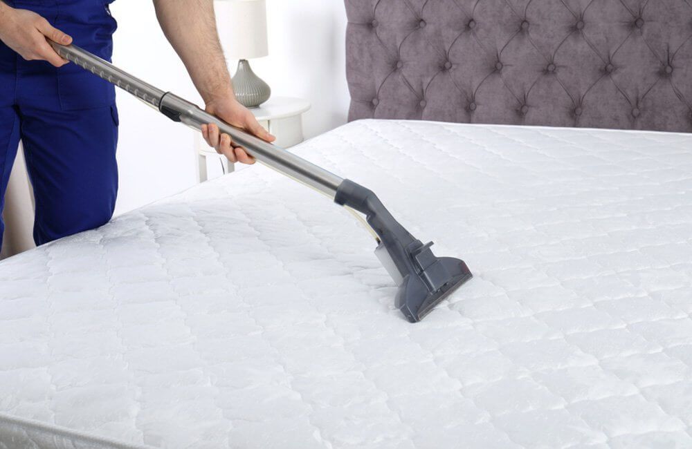 A man is cleaning a mattress with a vacuum cleaner.
