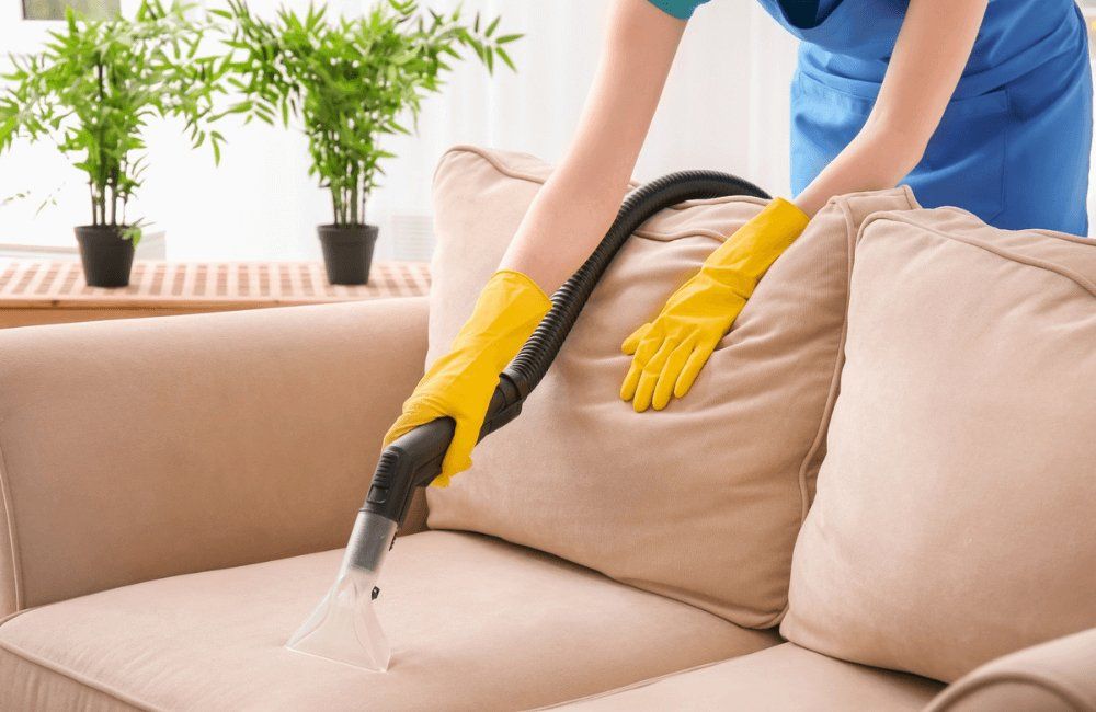 A woman is cleaning a couch with a vacuum cleaner.
