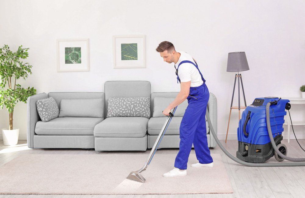 A man is using a vacuum cleaner to clean a carpet in a living room, preparing the surface for carpet steam cleaning process.