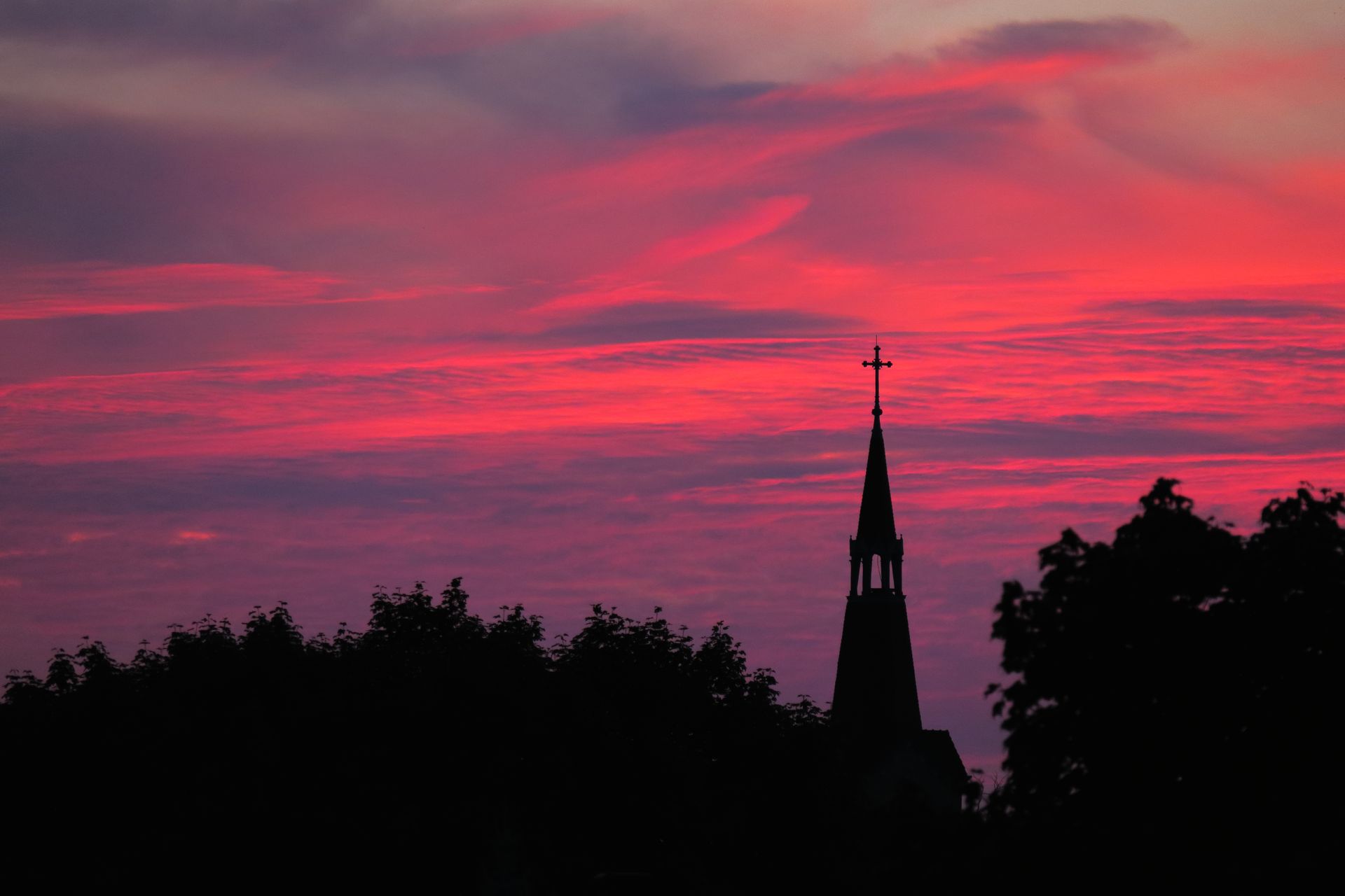 Silhouette of a church steeple against a vibrant pink and purple sunset sky.