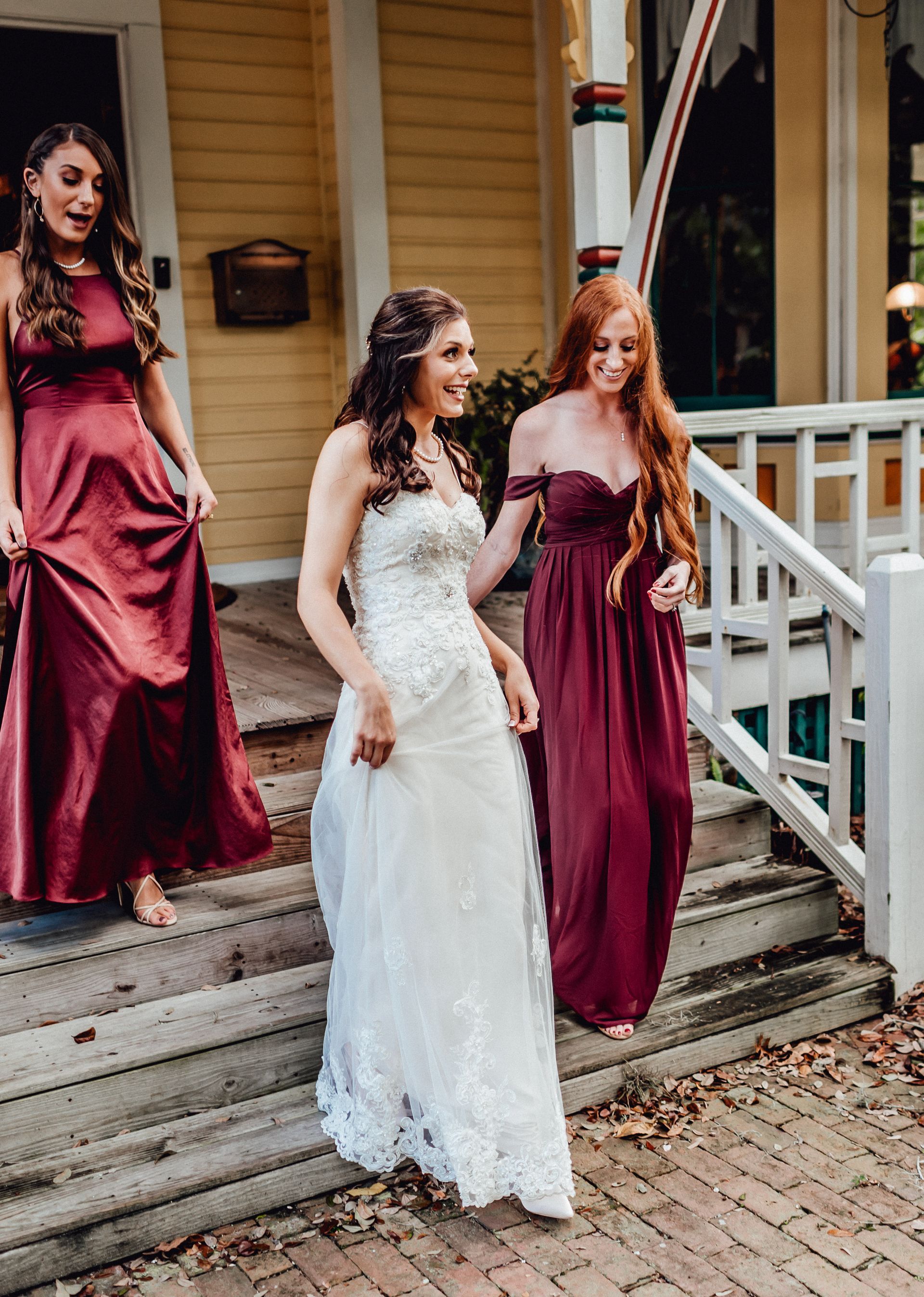 A bride and 2 bridesmaids walking down the stairs of the Laurel Oak Inn porch.
