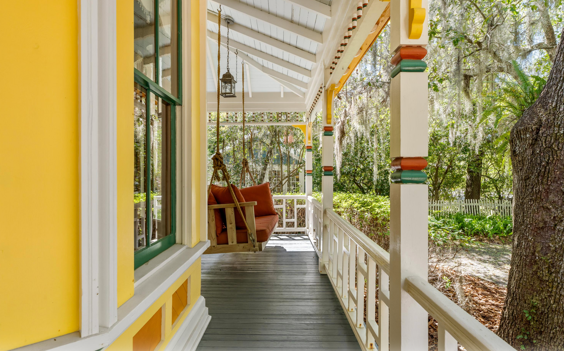 The Front porch of a yellow Victorian home with a swing