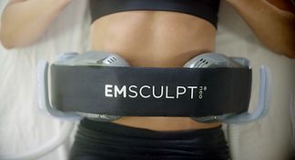 A woman is laying on a bed with a belt around her waist that says emsculpt.