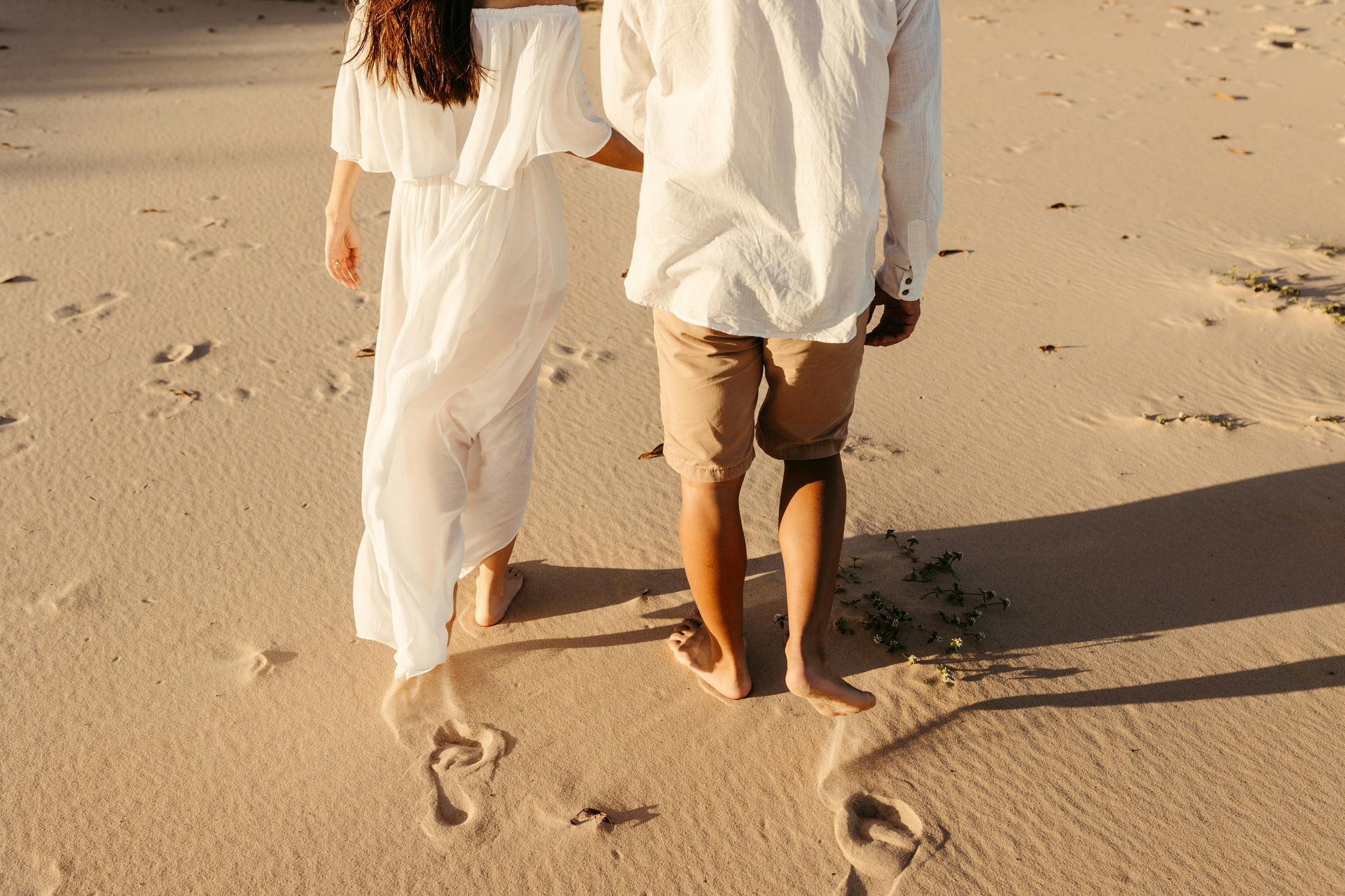 A man and a woman are walking barefoot on the beach.