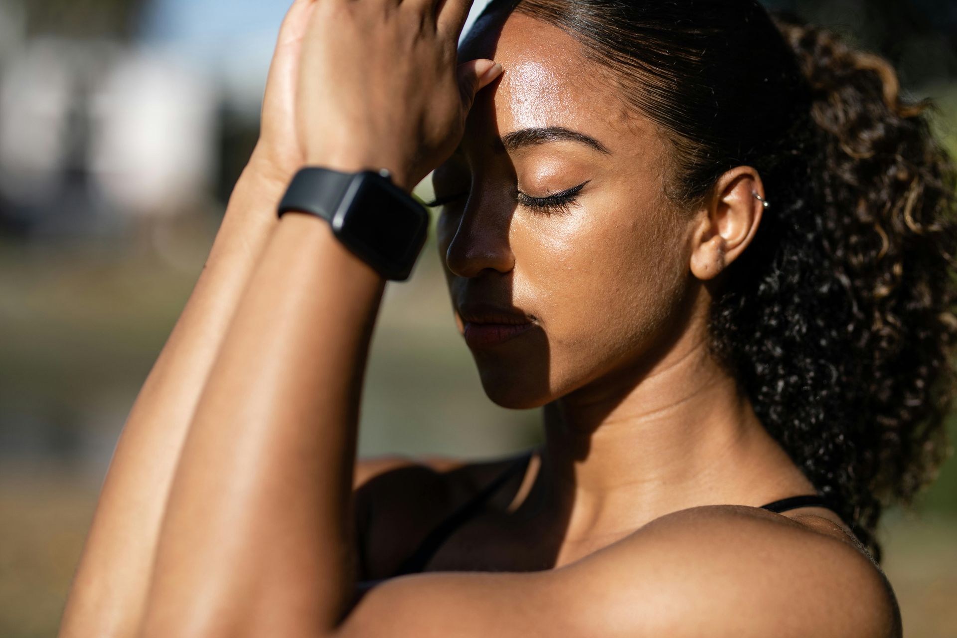 A woman wearing a smart watch is holding her head.