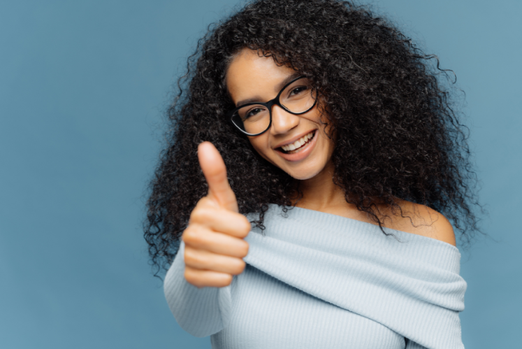A woman with curly hair and glasses is giving a thumbs up.